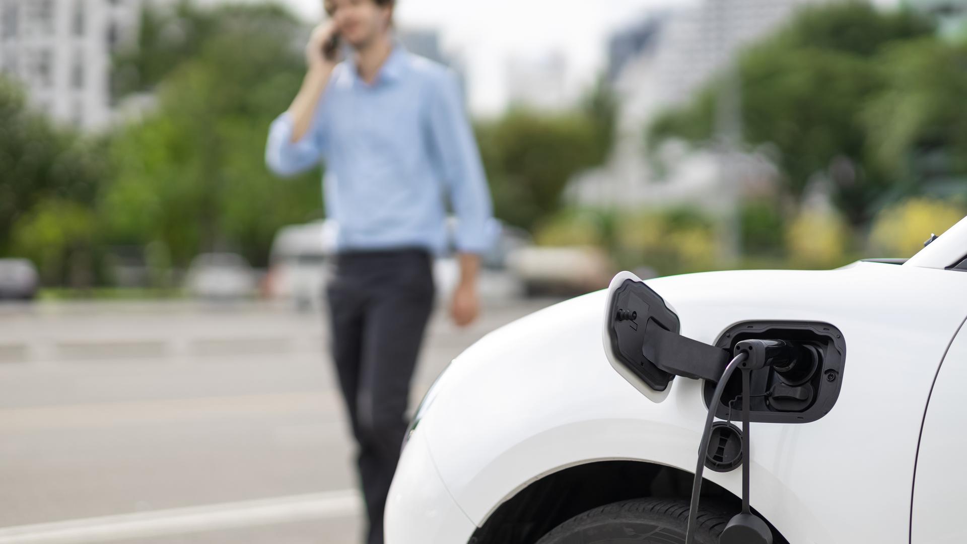 Ein E-Auto lädt während ein Mann daneben telefoniert.