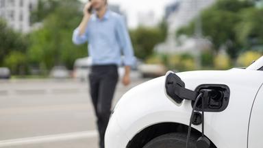 Ein E-Auto lädt während ein Mann daneben telefoniert.
