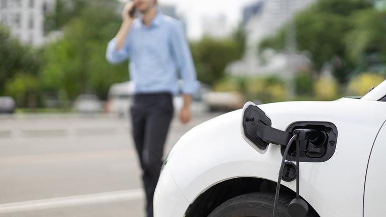 Ein E-Auto lädt während ein Mann daneben telefoniert.