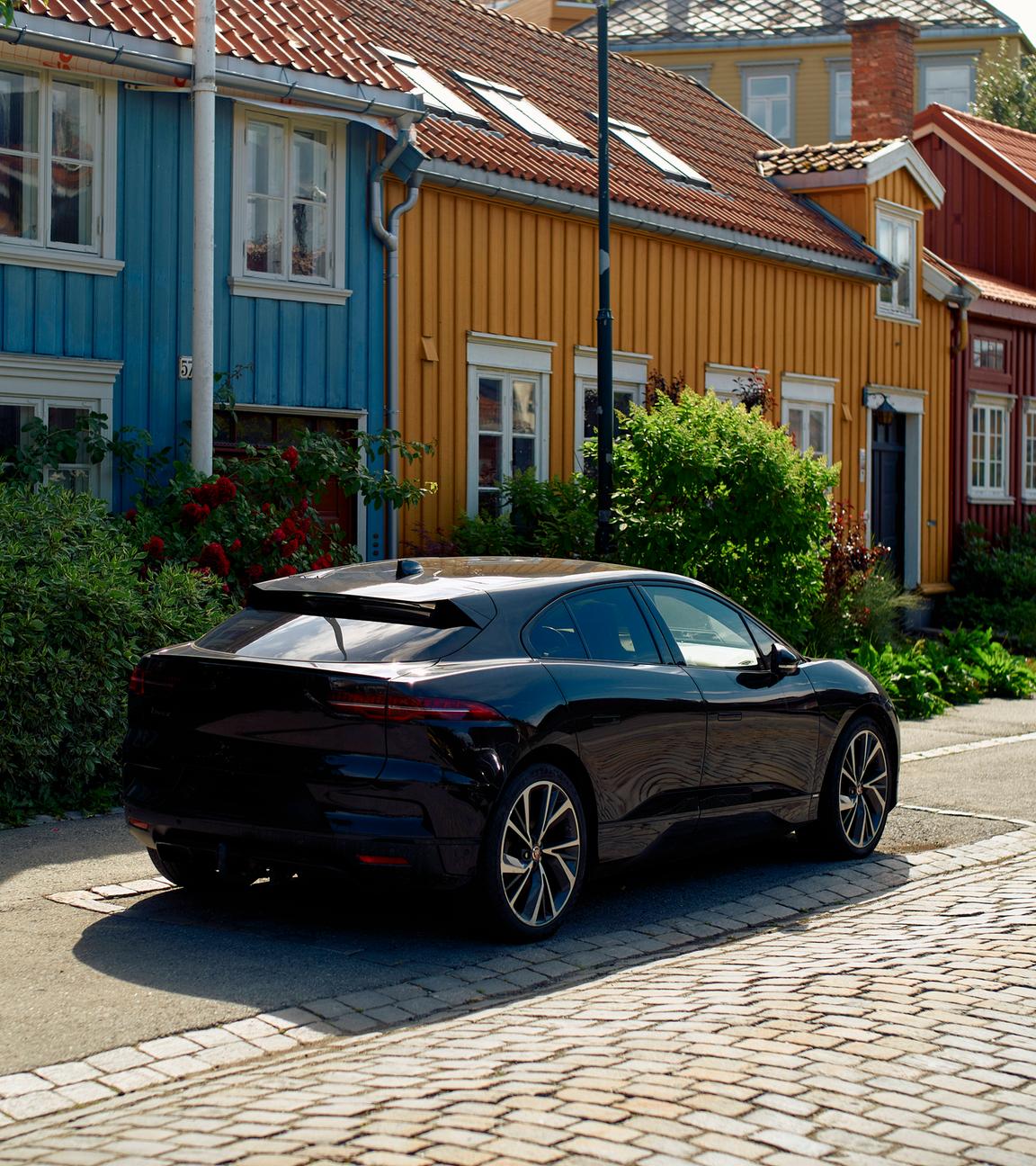 Ein schwarzes Elektroauto steht vor bunten Holzhäusern im norwegischen Trondheim.