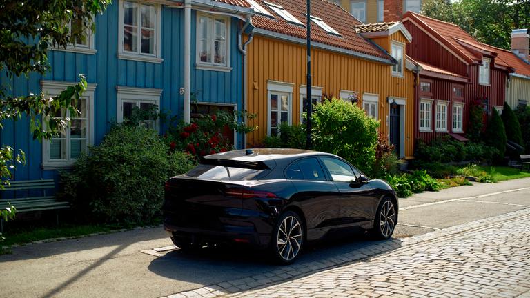 Ein schwarzes Elektroauto steht vor bunten Holzhäusern im norwegischen Trondheim.