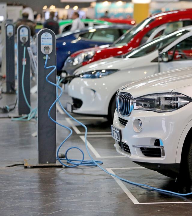 Mehrere E-Autos stehen neben einander uns sind an Ladestationen angeschlossen.