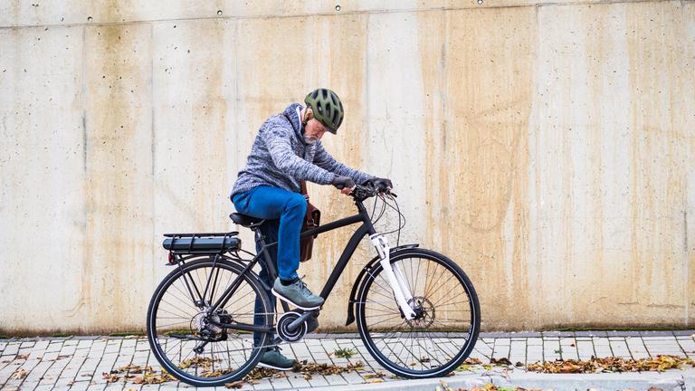 Senior mit Helm steigt auf E-Bike am Straßenrand.