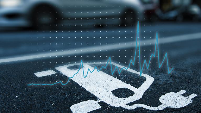 Über einem Parkplatz für E-Autos ist eine Liniengrafik eingeblendet, die zeigt, wie die Verkaufszahlen für E-Autos zuletzt gesunken sind.