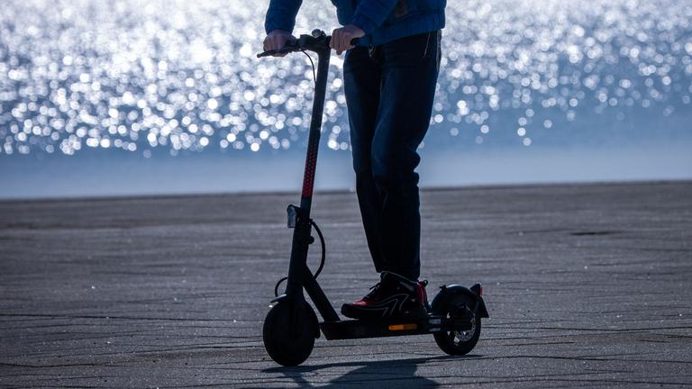 Ein Fahrer ist mit einem E-Scooter am Hafen unterwegs.