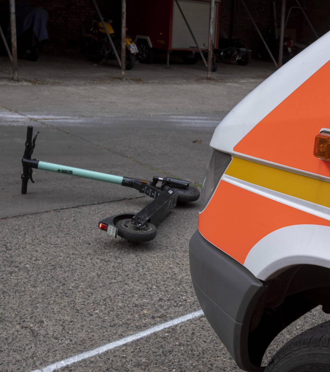 Ein auf der Straße liegender E-Roller vor einem Rettungswagen.