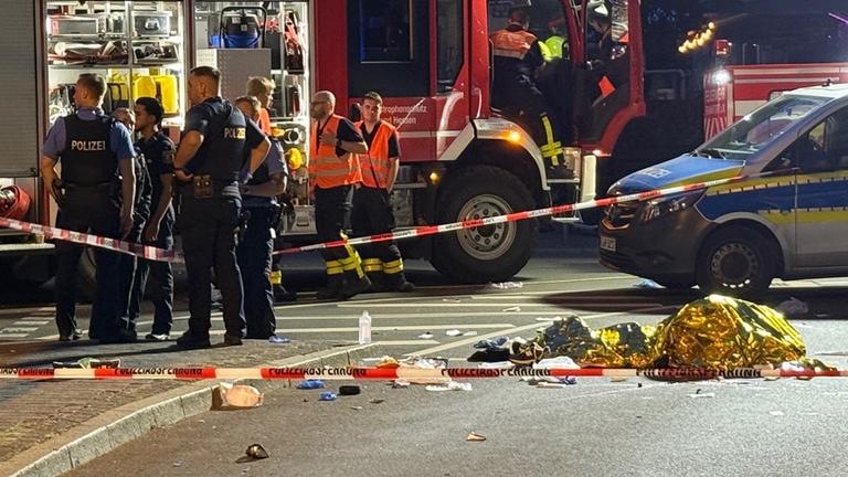  Einsatzkräfte der Polizei und Feuerwehr stehen am Unfallort an dem ein Autofahrer in der Nacht vom 06.07.2025 eine Person auf einem E-Scooter erfasst.