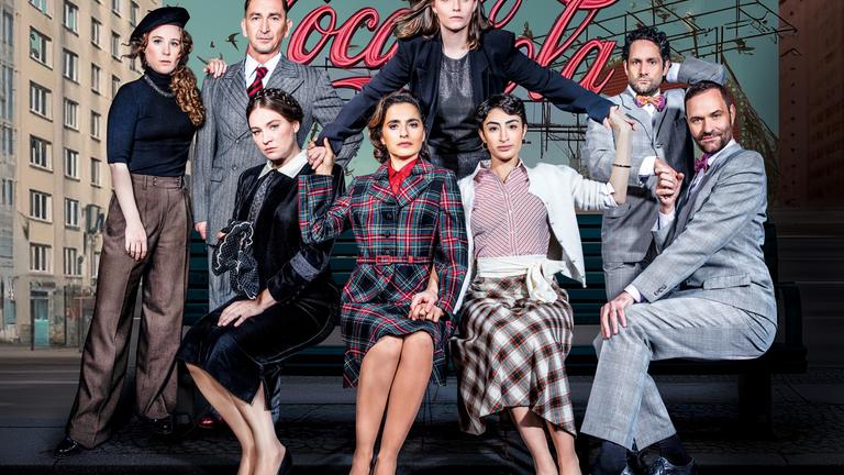 Auf dem Gruppenfoso sitzen drei Frauen und ein Mann in Business-Kleidung auf einem Sofa, hinter ihnen stehen nochmals zwei Frauen und Zwei Männer.