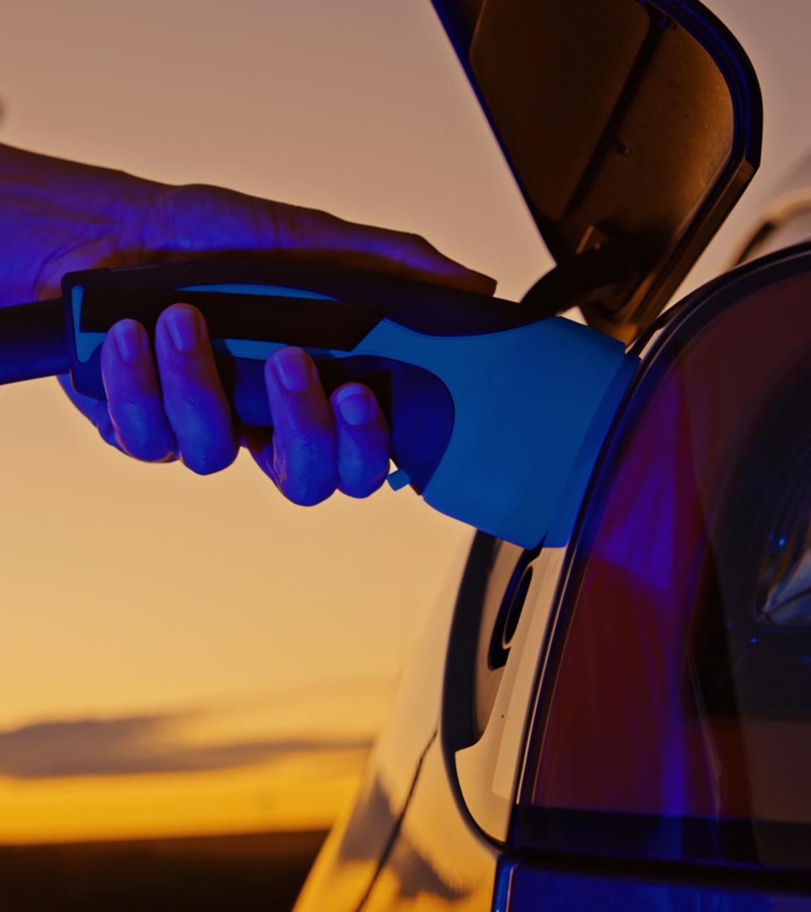 Hand betankt ein Elektroauto mit Strom im Sonnenuntergang