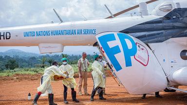 Einige Männer in Schutzkleidung verfrachten medizinische Hilfsgüter in einen Helikopter der Vereinten Nationen.