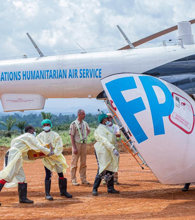 Einige Männer in Schutzkleidung verfrachten medizinische Hilfsgüter in einen Helikopter der Vereinten Nationen.