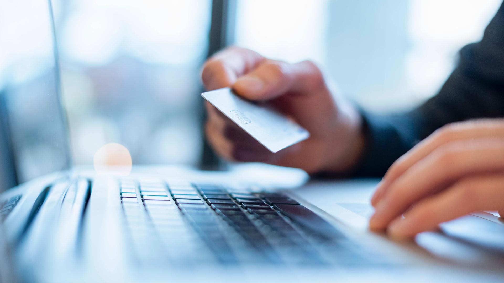 Mann hält eine Bankkarte über einer Laptop-Tastatur.