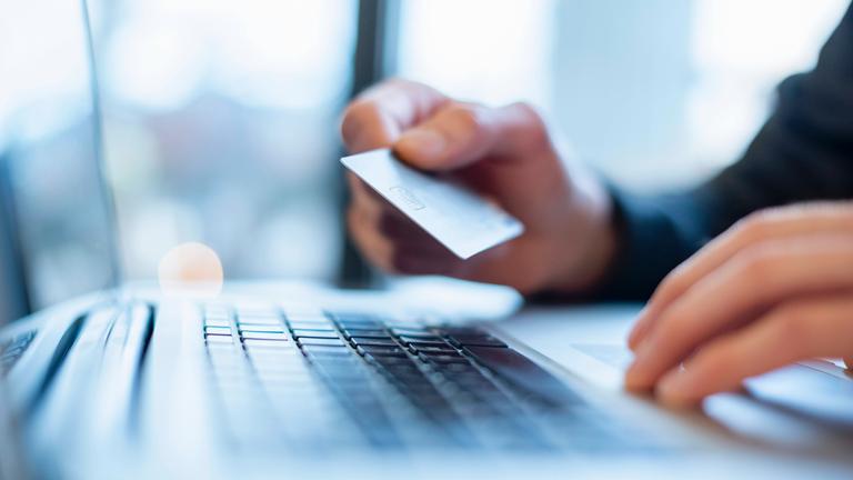 Mann hält eine Bankkarte über einer Laptop-Tastatur.