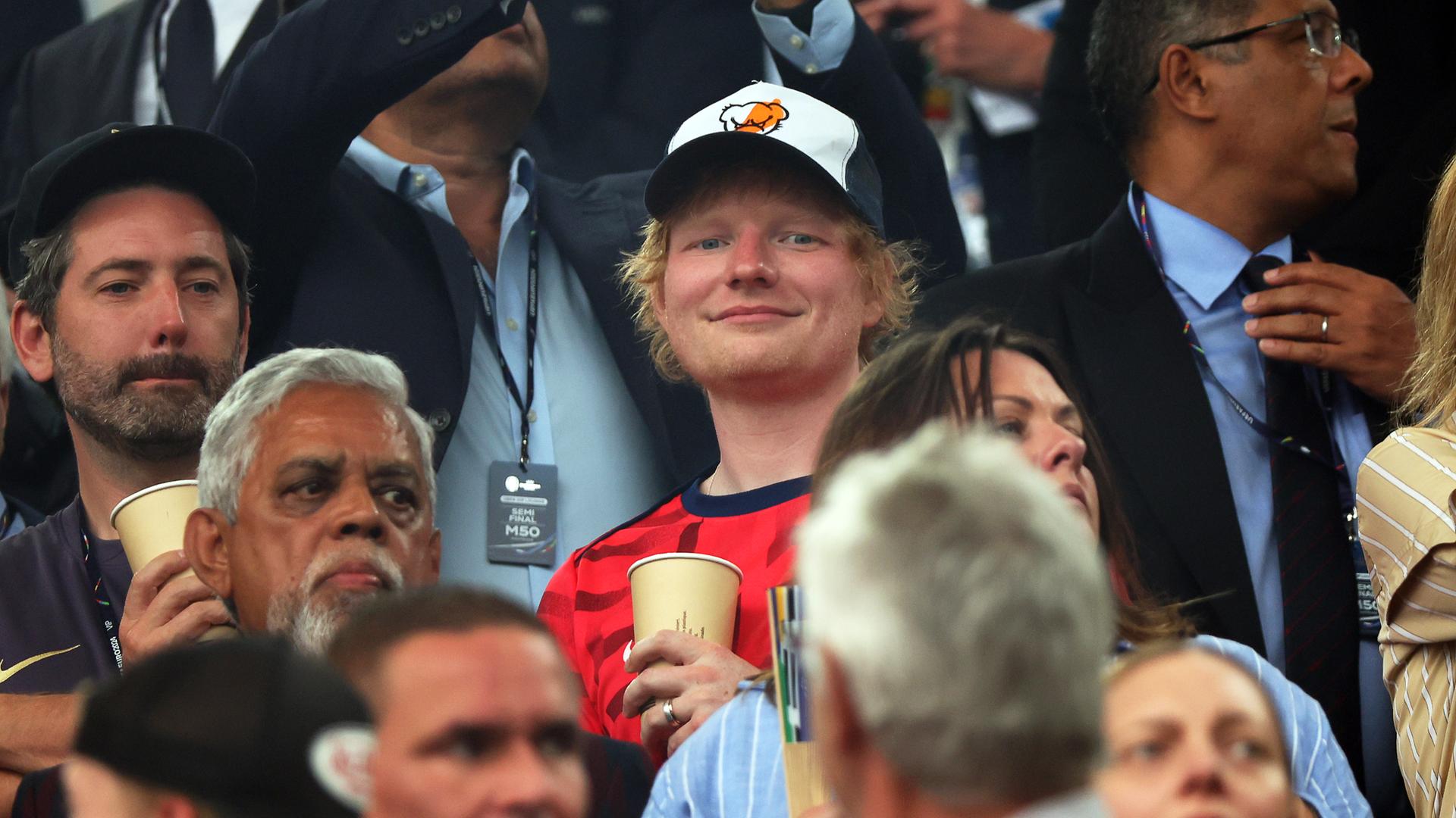 Ed Sheeran (M), Sänger aus Großbritannien, steht vor Spielbeginn auf der Tribüne.