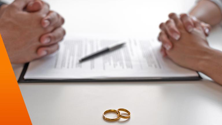 Jeweils gefaltete Hände von Mann und Frau mit Vertrag in der Mitte, davor Eheringe