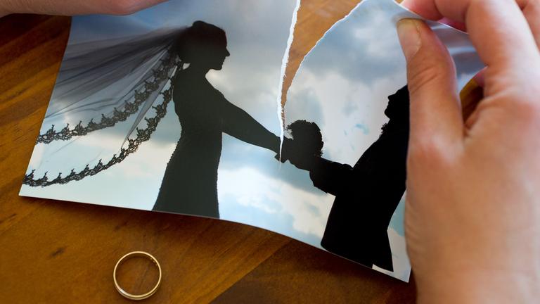 Hände zereißen ein Hochzeitsfoto, unter dem Foto liegt ein Ehering.