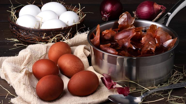 Natürlich gefärbte Eier in einem Korb, daneben steht ein Topf mit einem Sud aus Zwiebelschalen.