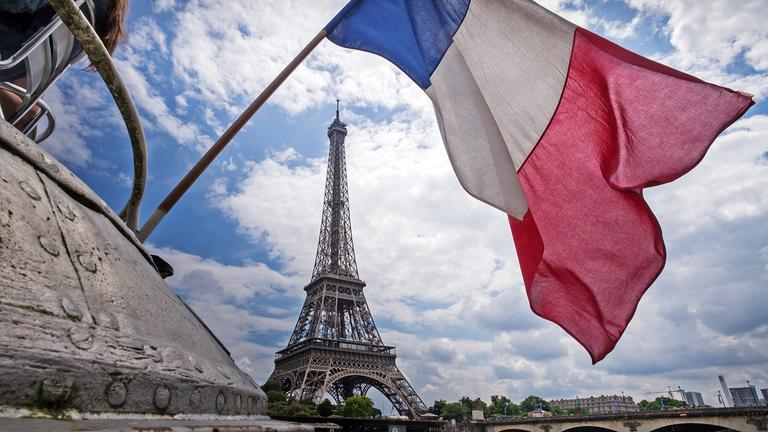 Die französische Flagge weht am heck eines Schiffes vor dem Eiffelturm in Paris (Frankreich)