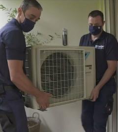 Zwei Männer tragen das Außengerät einer Klimaanlage auf einen Balkon