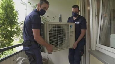 Zwei Männer tragen das Außengerät einer Klimaanlage auf einen Balkon