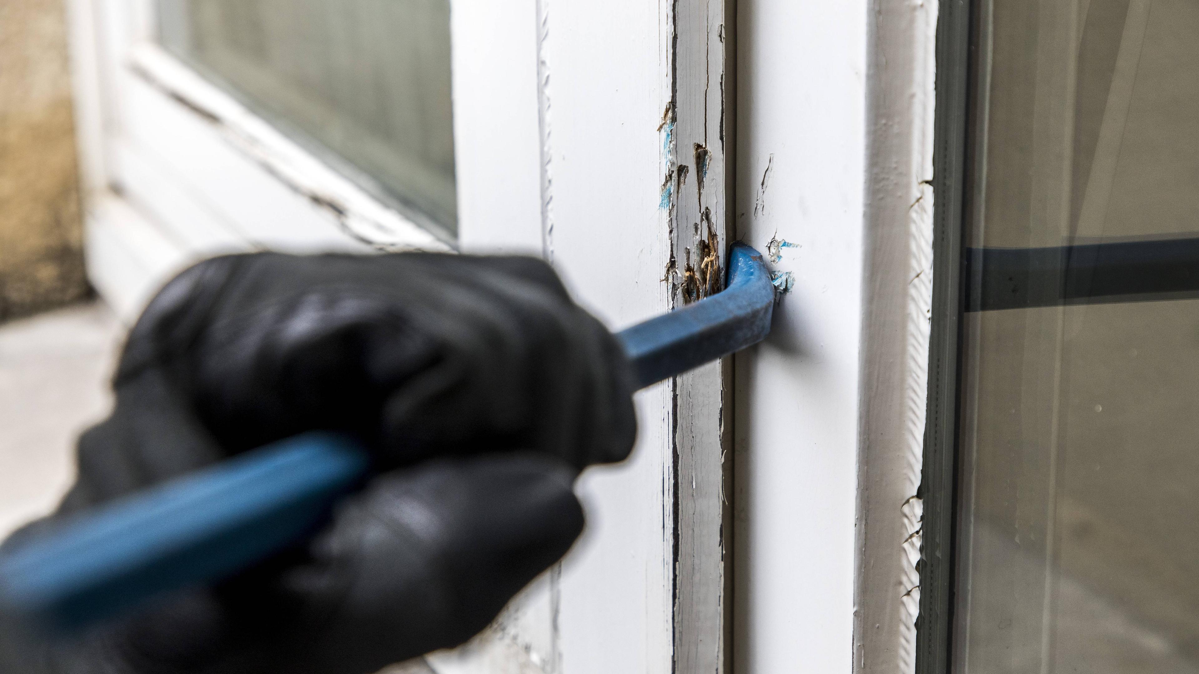 Ein Mann mit schwarzen Handschuhen versucht, ein Fenster mit einer Brechstange aufzustemmen.