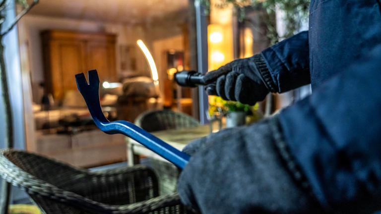 Einbrecher mit Brecheisen vor einem Fenster
