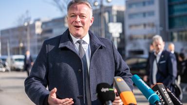 Gordon Schnieder freut sich und spricht in einige Mikrofone. 