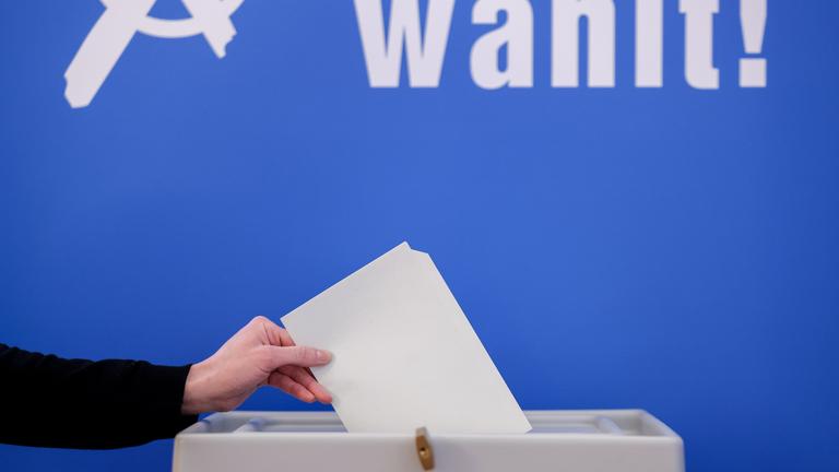 Ein Wahlzettel wird in eine Wahlurne gesteckt.