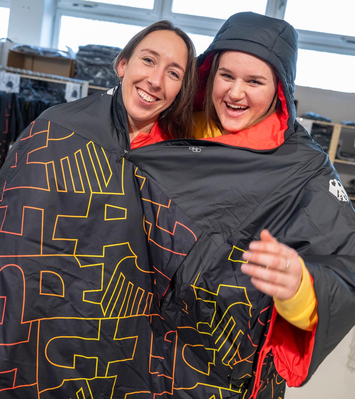 Kira Weidle-Winkelmann (l.) und Emma Aicher teilen sich während der Einkleidung für die Winterspiele in Mailand aus Spaß einen Poncho