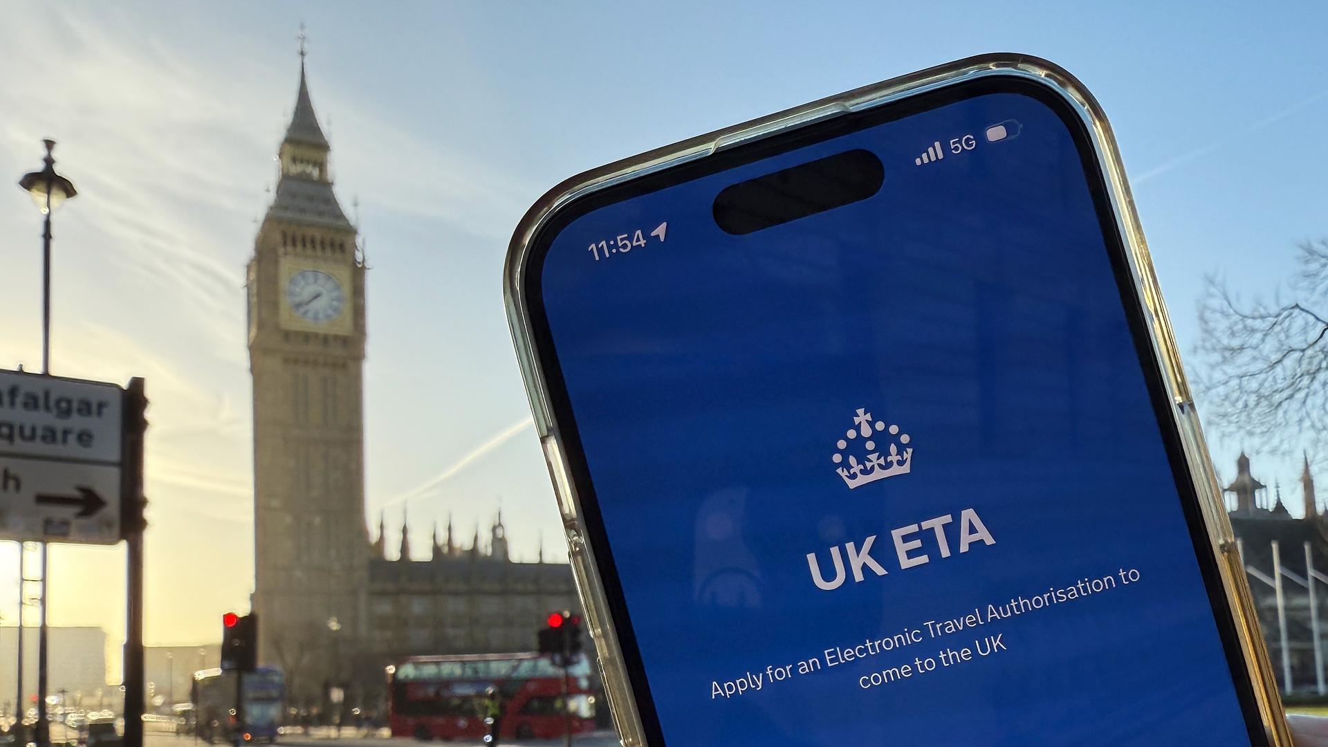 Ein Mobiltlefon mit der App der britischen Regierung zur Beantragung der Einreisegenehmigung ETA wird vor dem Elizabeth Tower gehalten