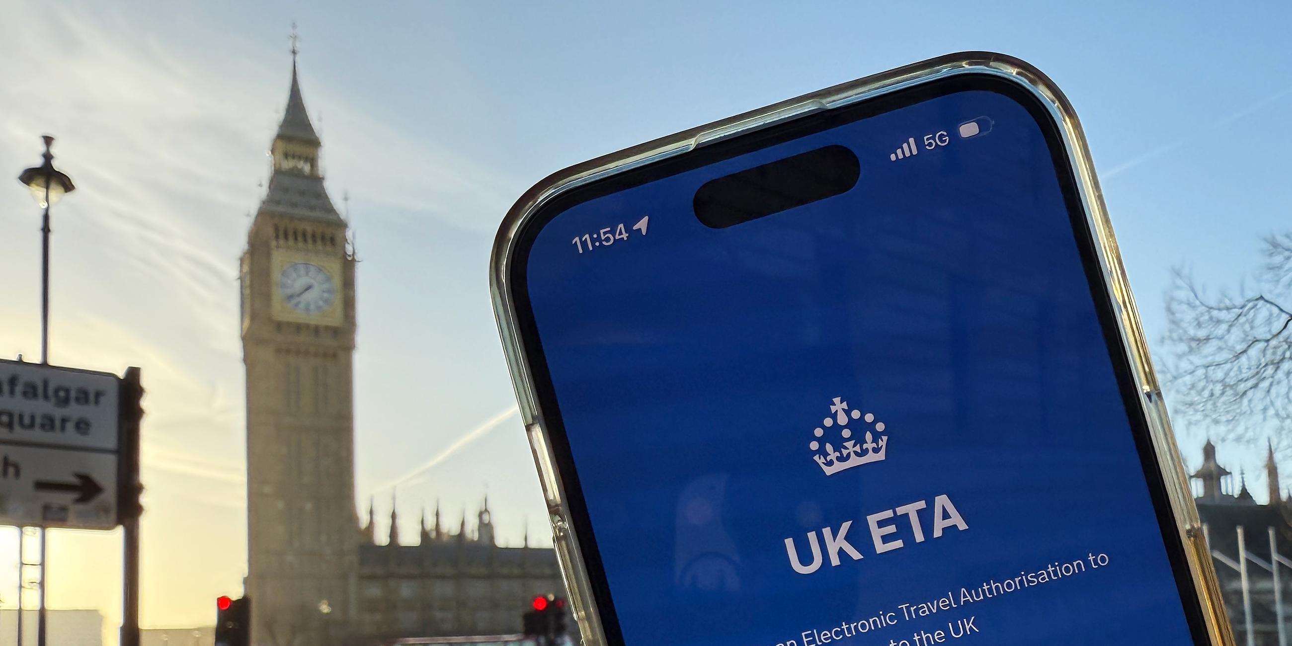 Ein Mobiltlefon mit der App der britischen Regierung zur Beantragung der Einreisegenehmigung ETA wird vor dem Elizabeth Tower gehalten