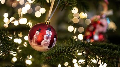 Niedersachsen, Göttingen: Eine Weihnachtskugel hängt an einem Weihnachtsbaum mit einer Lichterkette.
