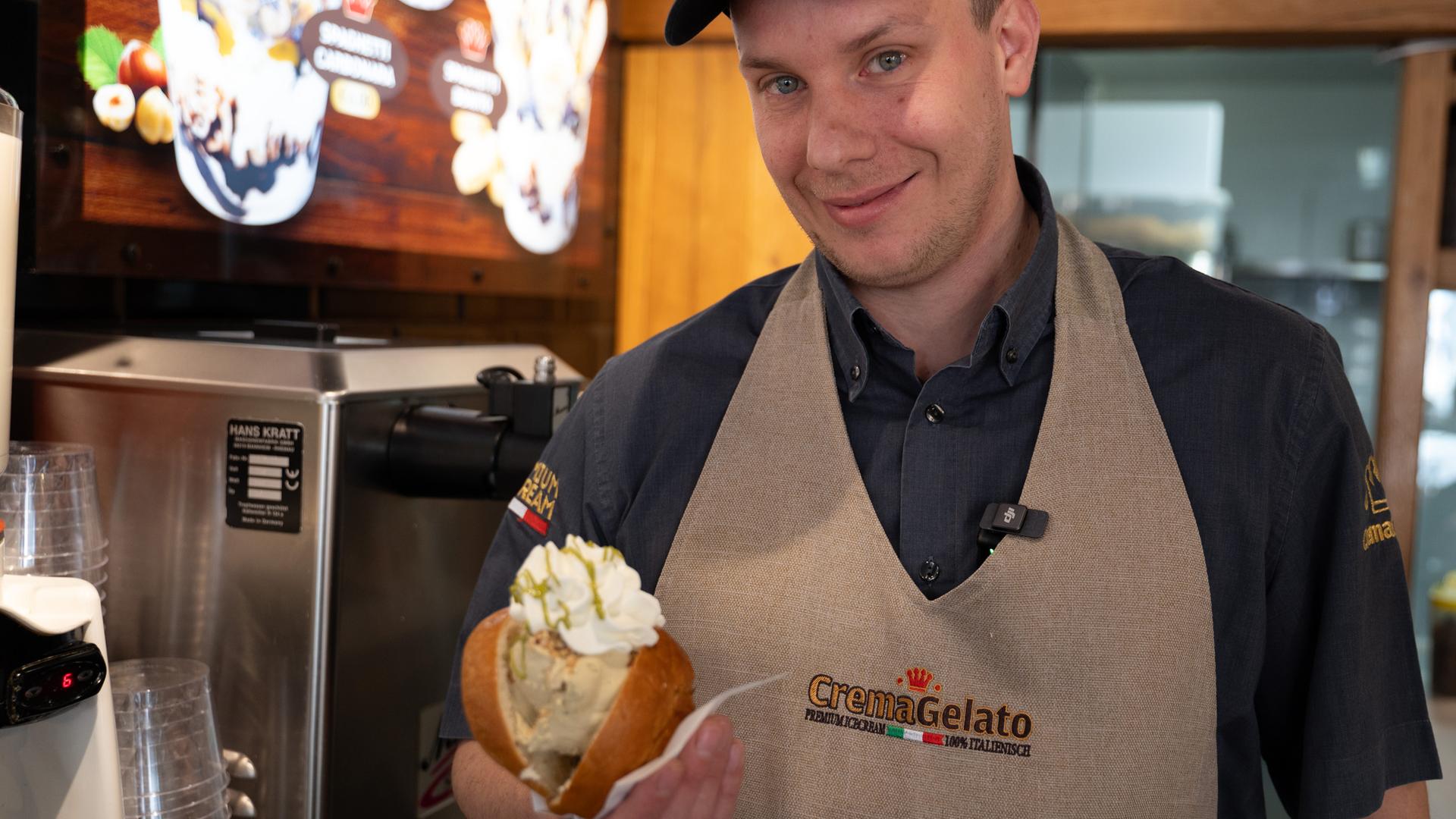 Baden-Württemberg, Baden-Baden: Eisdielenbesitzer Marco Caimmi hält ein Brioche Brötchen mit zwei Kugeln Eis in der Hand.