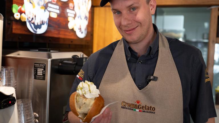Baden-Württemberg, Baden-Baden: Eisdielenbesitzer Marco Caimmi hält ein Brioche Brötchen mit zwei Kugeln Eis in der Hand.