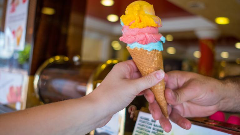 Mitarbeiterin eines Eiscafés übergibt Frau Eis in einer Waffel.