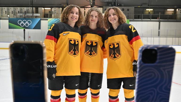 Die deutschen Eishockey-Spielerinnen Luisa Welcke, Svenja Voigt und Lilli Welcke (von links) posieren vor zwei Smartphones.
