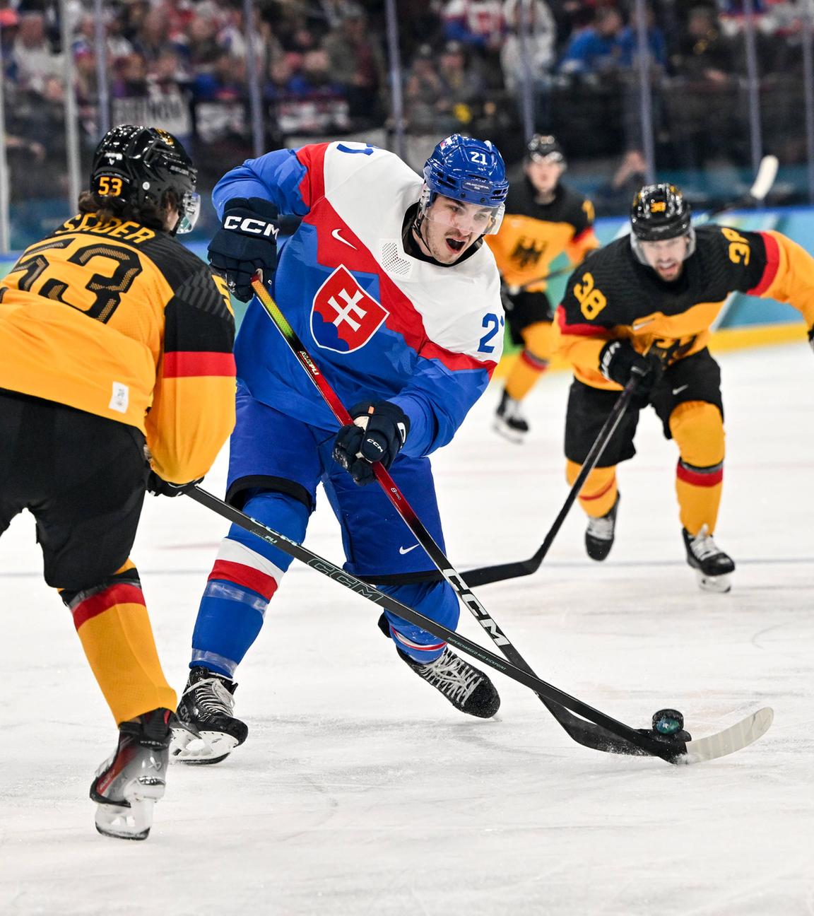 Der slowakische Eishockeyspieler Adam Ruzicka versucht im Zweikampf, den Puck mit dem Schläger an Deutschlands Nationalspieler Moritz Seider vorbeizulupfen