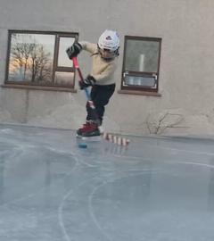 Ein Kind spielt Eishockey auf Eisfläche im Garten.