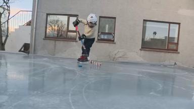 Ein Kind spielt Eishockey auf Eisfläche im Garten.