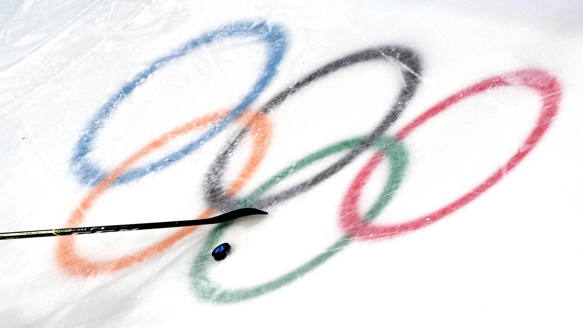 Die olympischen Ringe im Eis mit Puk und Schläger.