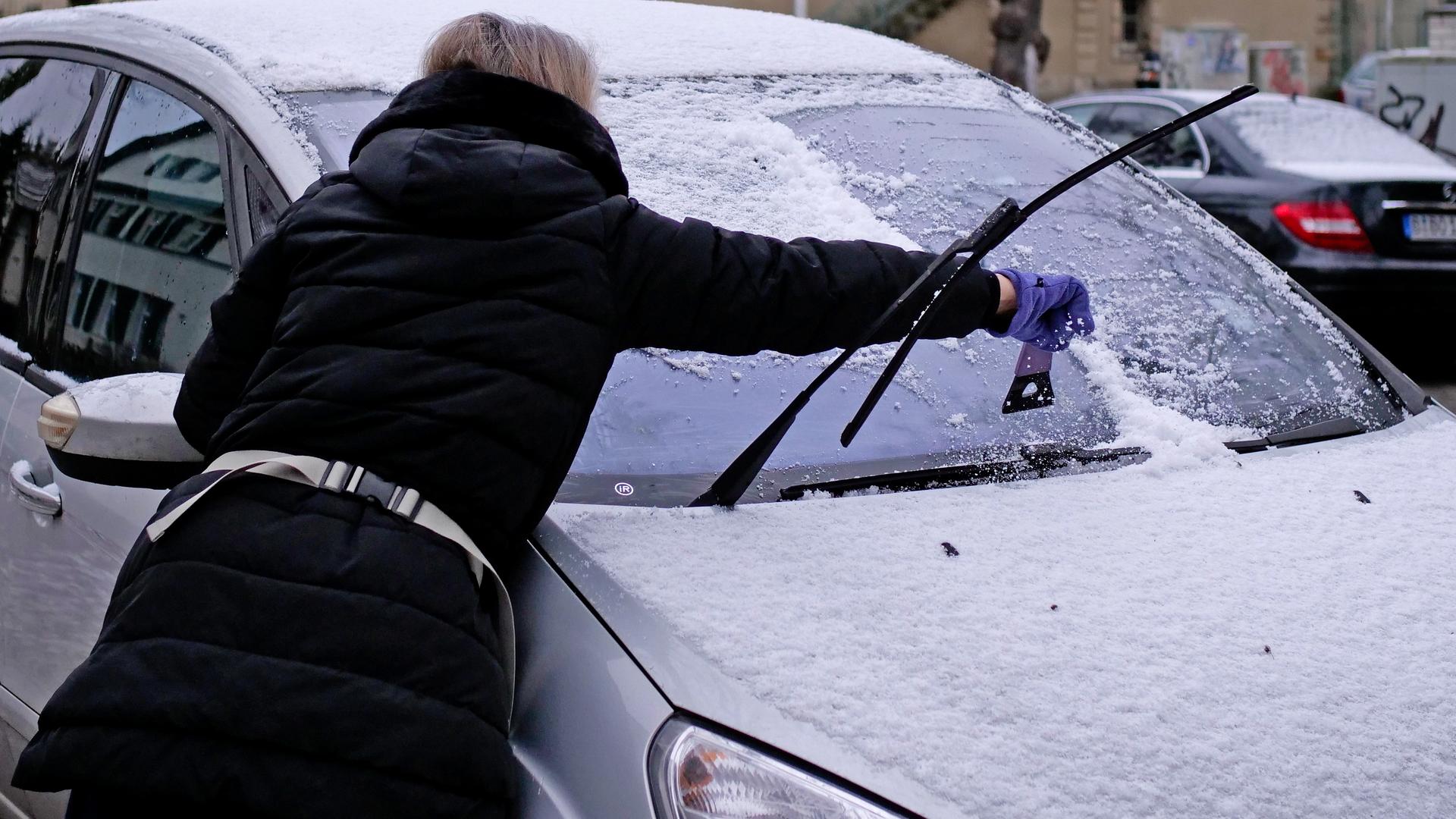 Eine Frau entfernt mit einem Eiskratzer Schnee und Eis von der Frontscheibe ihres Autos.
