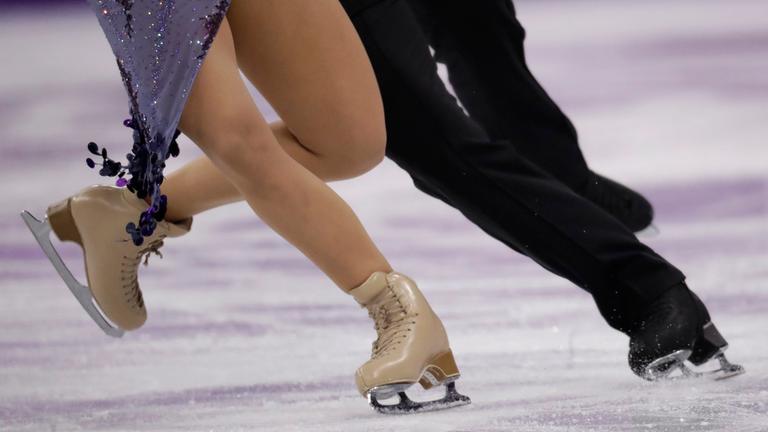 Die Beine eines Eiskunstlaufpaares bei der Fahrt auf dem Eis.