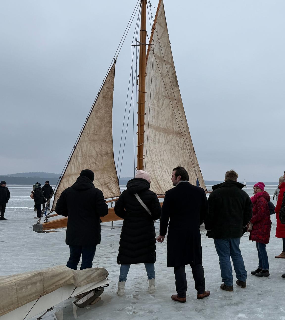 Die Eissegelyacht "Papagena" auf dem Müggelsee, davor stehen einige Menschen und schauen auf das Boot.