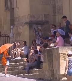 Eine Gruppe von Menschen sitzt im Schatten während eine Frau mit einem Regenschirm sich von der Sonne schützt
