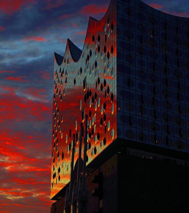 In der Glasfassade der Elbphilharmonie in Hamburg spiegelt sich das Abendlicht.