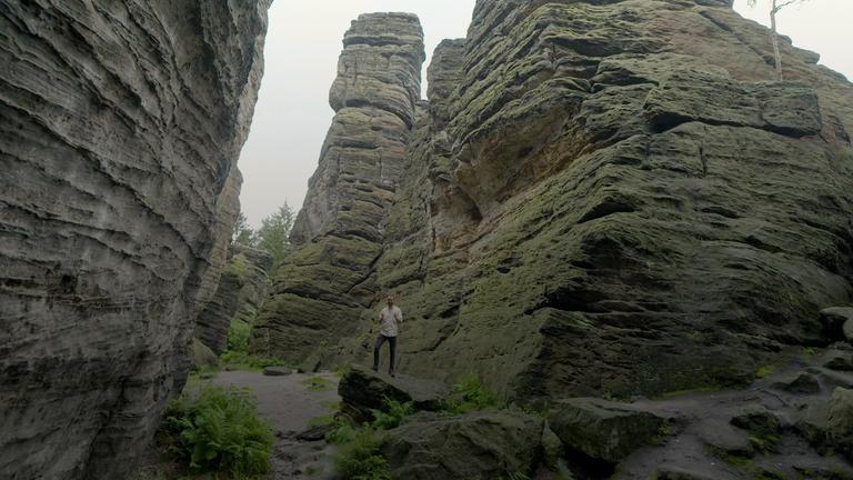 Mann steht zwischen Felsformationen im Elbsandsteingebirge.