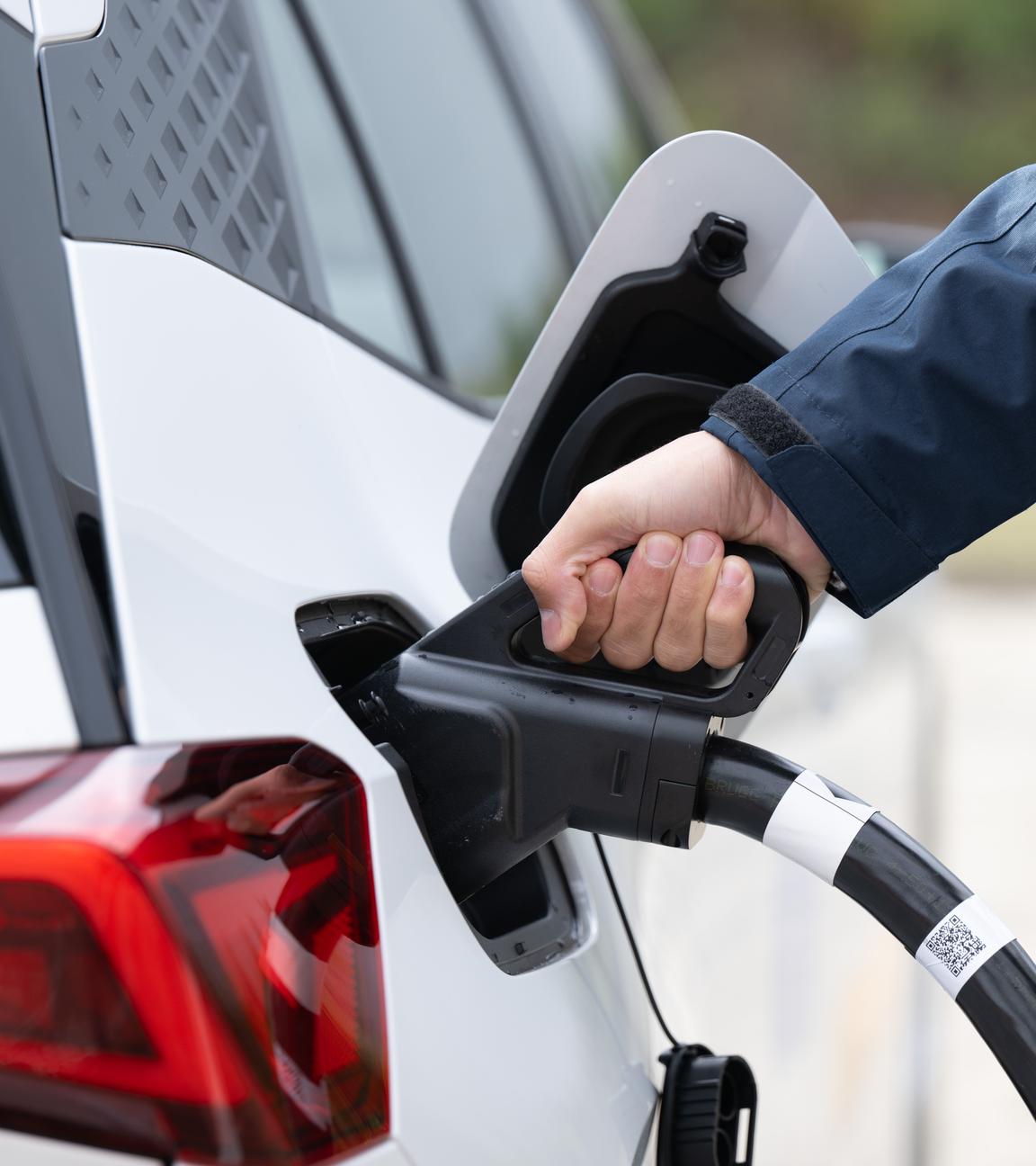  Ein Mann steckt ein Ladekabel in den Tankstutzen eines Elektroautos.
