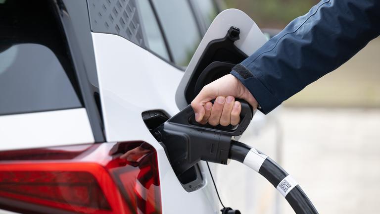  Ein Mann steckt ein Ladekabel in den Tankstutzen eines Elektroautos.