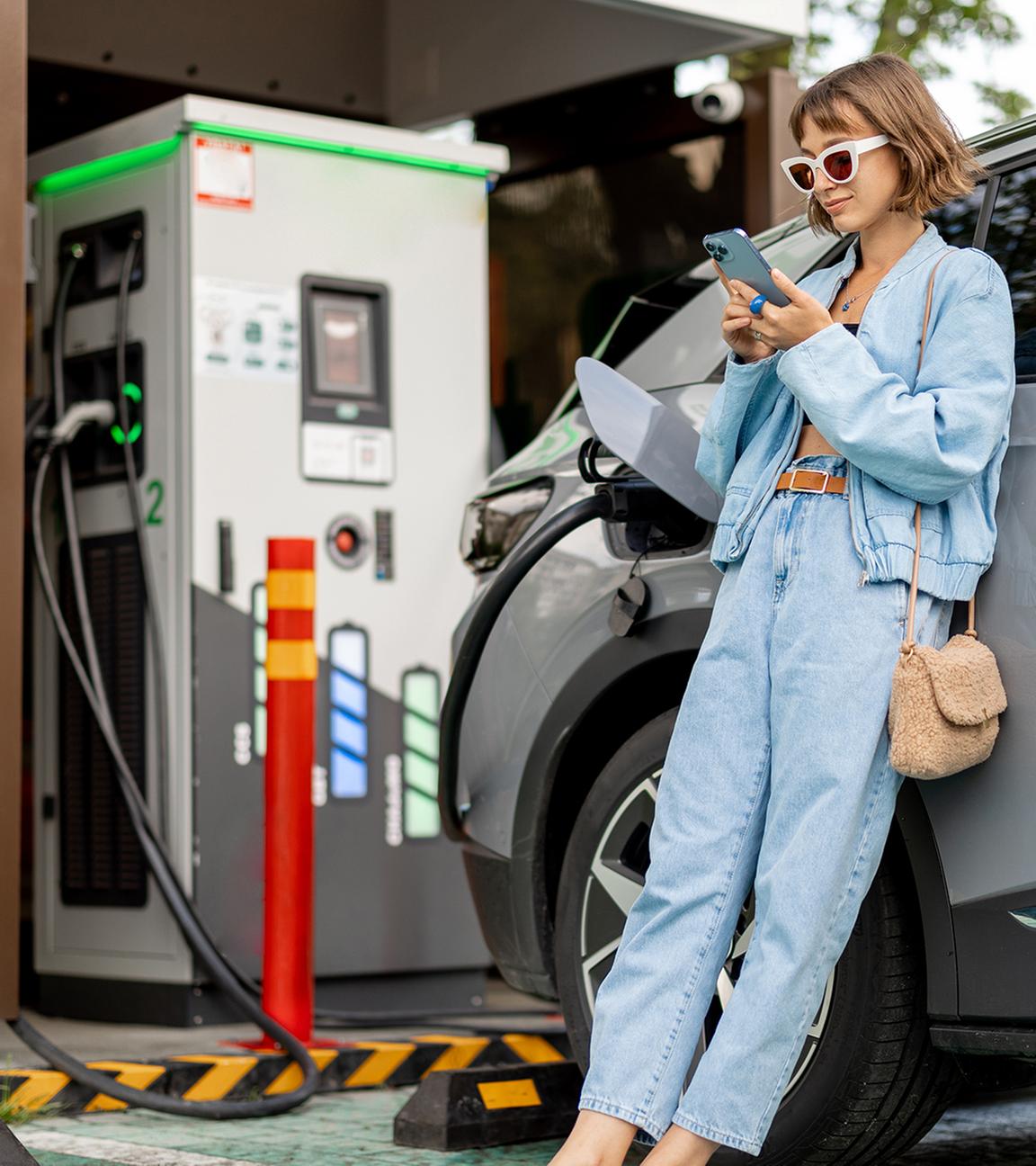 Frau lädt Elektroauto und schaut währendessen in ihr Smartphone