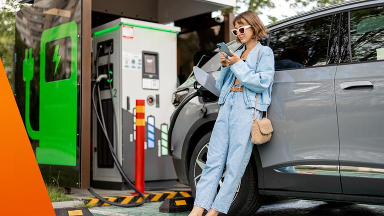 Frau lädt Elektroauto und schaut währendessen in ihr Smartphone